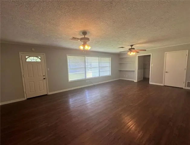 an empty room with wooden floor chandelier fan and windows