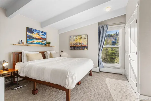 a spacious bedroom with a bed a dresser and painting on the wall