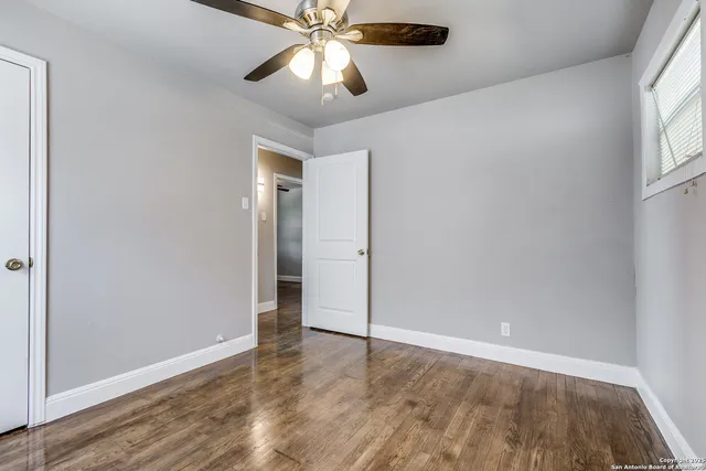 an empty room with wooden floor fan and windows
