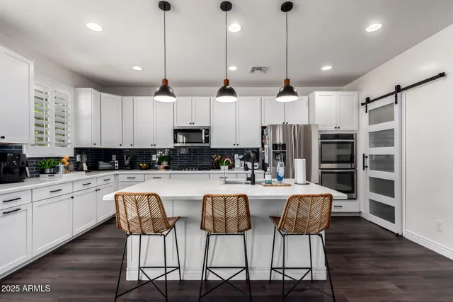 a large kitchen with granite countertop a dining table chairs stainless steel appliances and cabinets