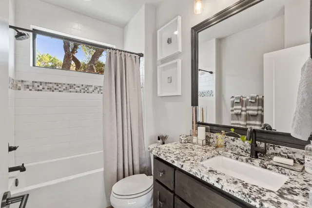 a bathroom with a granite countertop sink a toilet a mirror a vanity a bath tub and shower