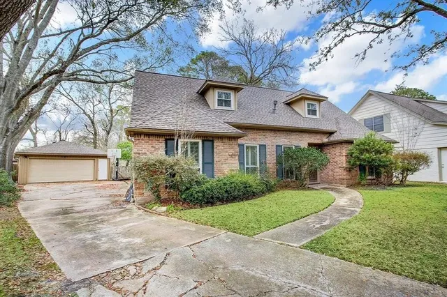 a view of a brick house with a yard plants and large tree