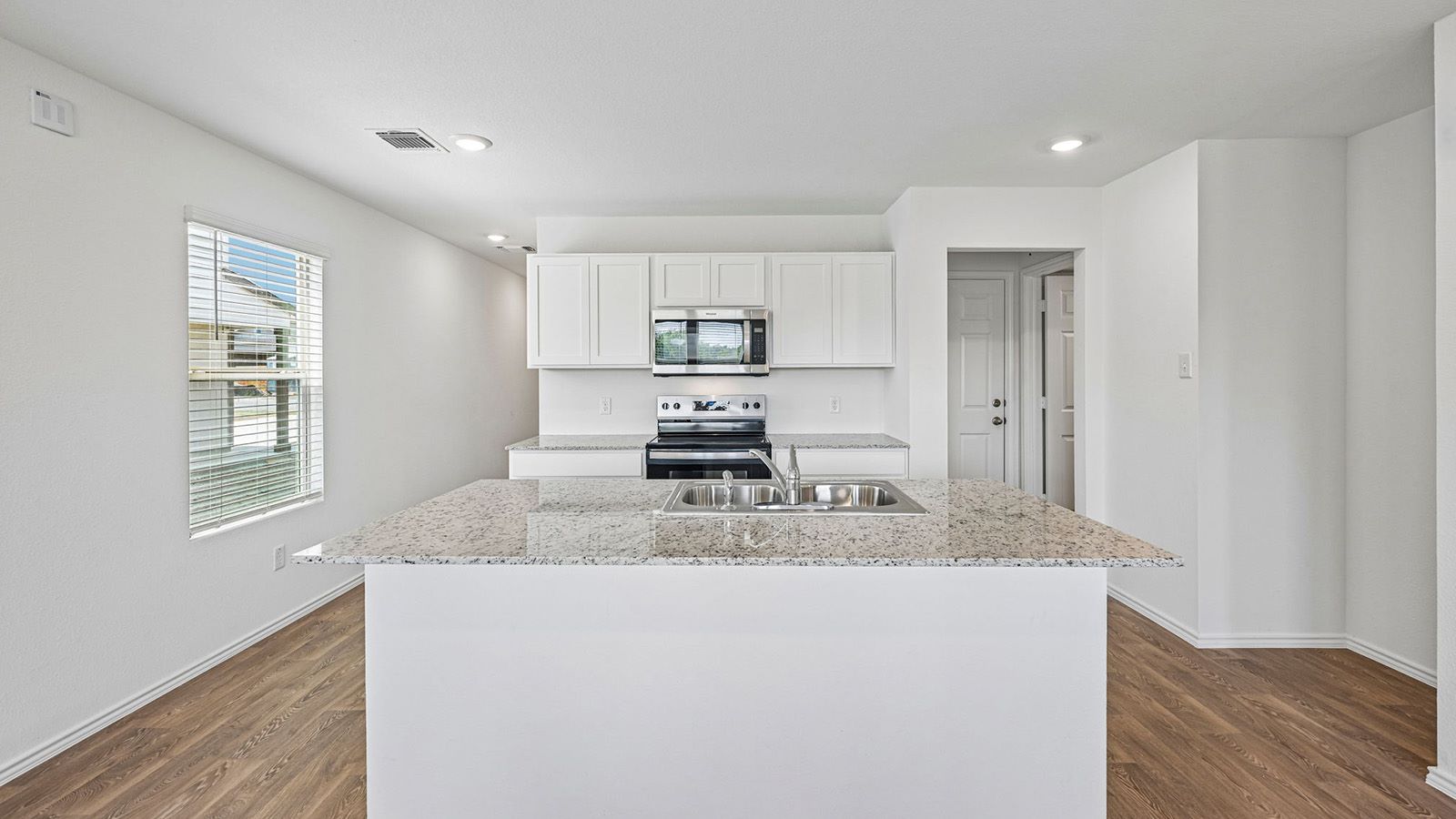 369 Old Stage Coach Road Jarrell, TX 76537 - Photo 4 of 25 Granite countertops and clean white cabinetry anchor this modern culinary workspace with warm wood flooring.