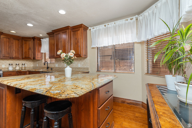 892 Cambridge Drive St. George, UT 84770 - Photo 26 of 65 Kitchen featuring a multi-toned granite island with seating, recessed lighting, wood-finish cabinetry, and a patterned tile backsplash