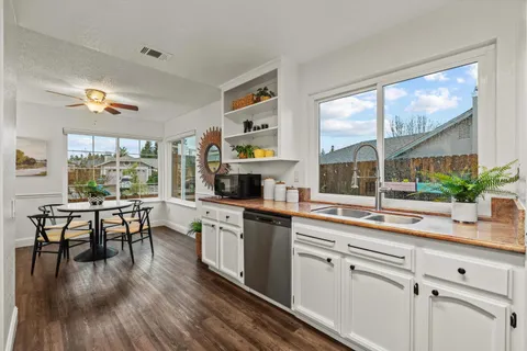 a kitchen with stainless steel appliances a stove a sink dishwasher a refrigerator white cabinets and wooden floor next to a window