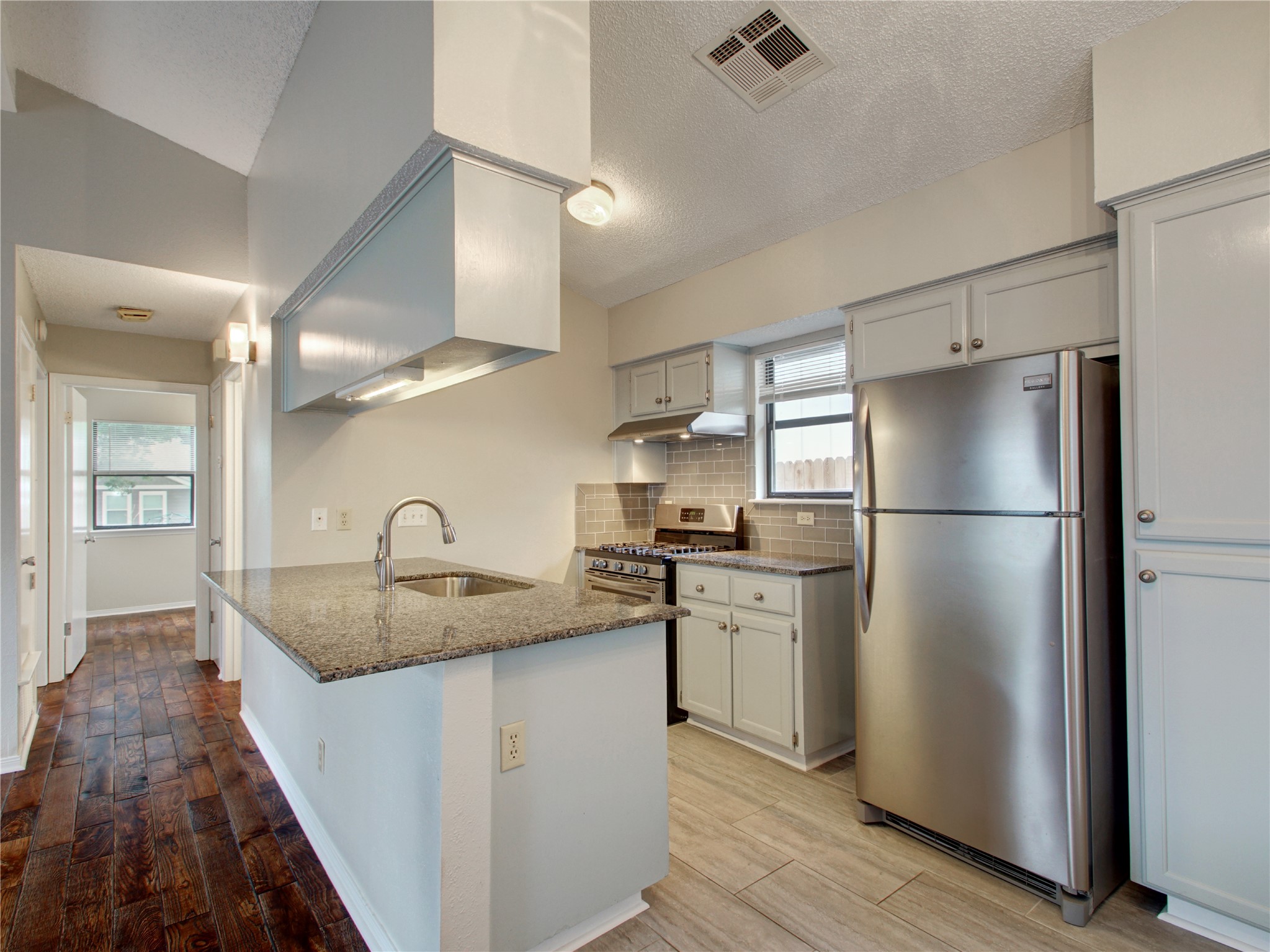 4703 Rosedale Avenue, Unit A Austin, TX 78756 - Photo 7 of 19 Kitchen featuring dark stone counters, appliances with stainless steel finishes, light wood-style flooring, tasteful backsplash, and a textured ceiling