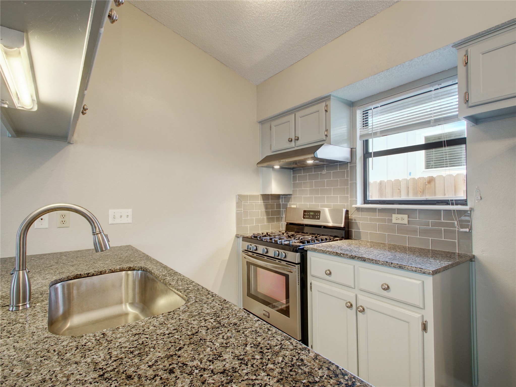 4703 Rosedale Avenue, Unit A Austin, TX 78756 - Photo 8 of 19 Kitchen with gas stove, under cabinet range hood, light stone countertops, a textured ceiling, and tasteful backsplash