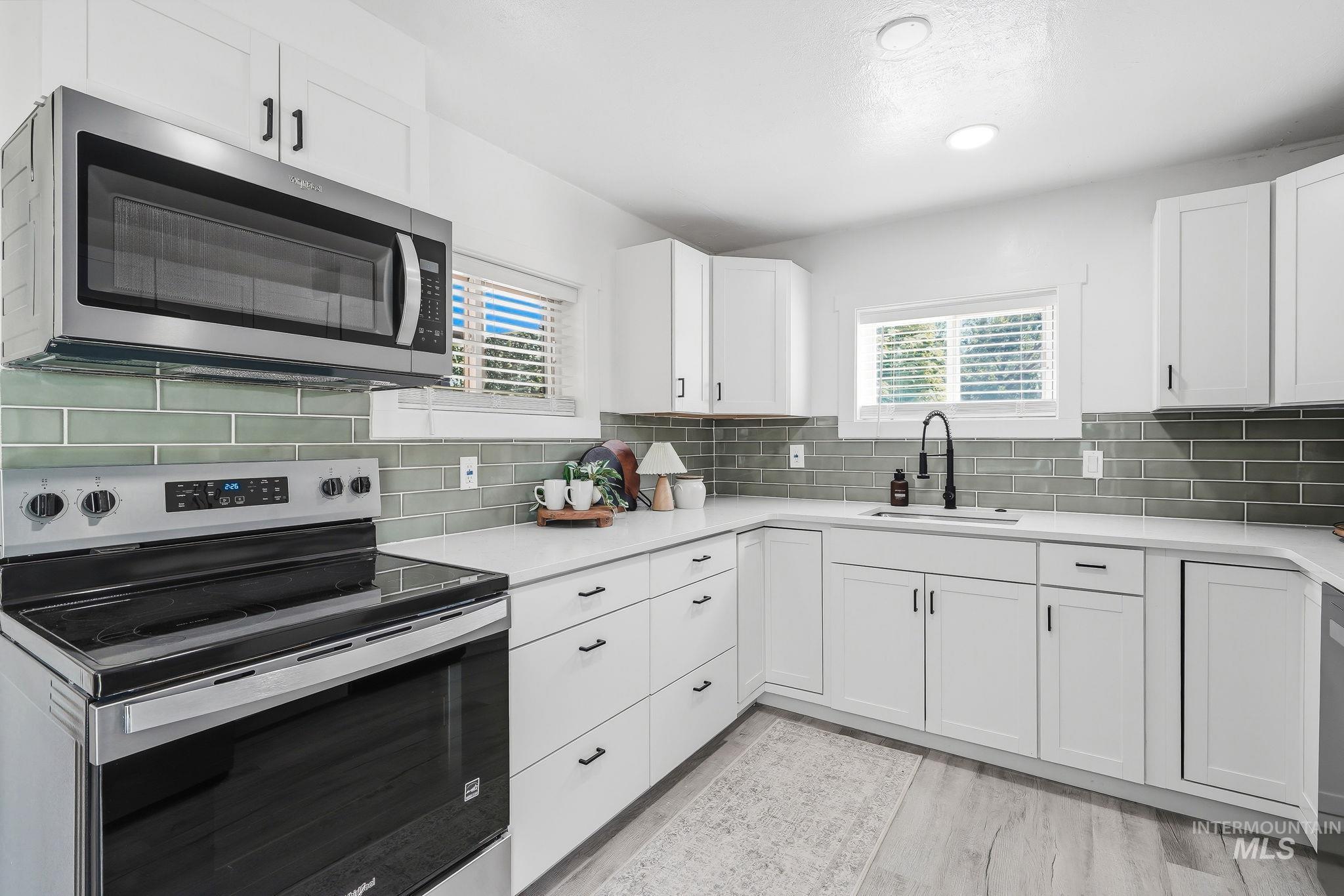 2152 Artesian Road Eagle, ID 83616 - Photo 16 of 50 Contemporary kitchen featuring white cabinetry, subway tile backsplash, stainless steel appliances, a built-in microwave, and wood-finish flooring