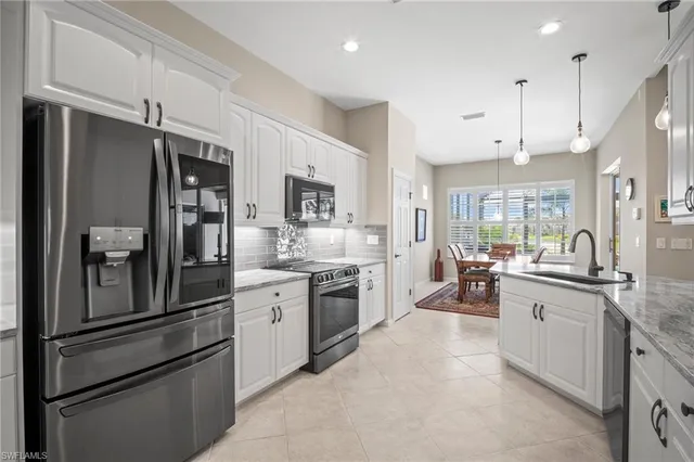 a kitchen with stainless steel appliances granite countertop a refrigerator a sink dishwasher a stove and white cabinets with wooden floor