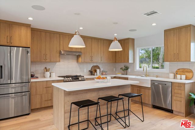 a kitchen with stainless steel appliances a sink a stove a refrigerator cabinets and wooden floor