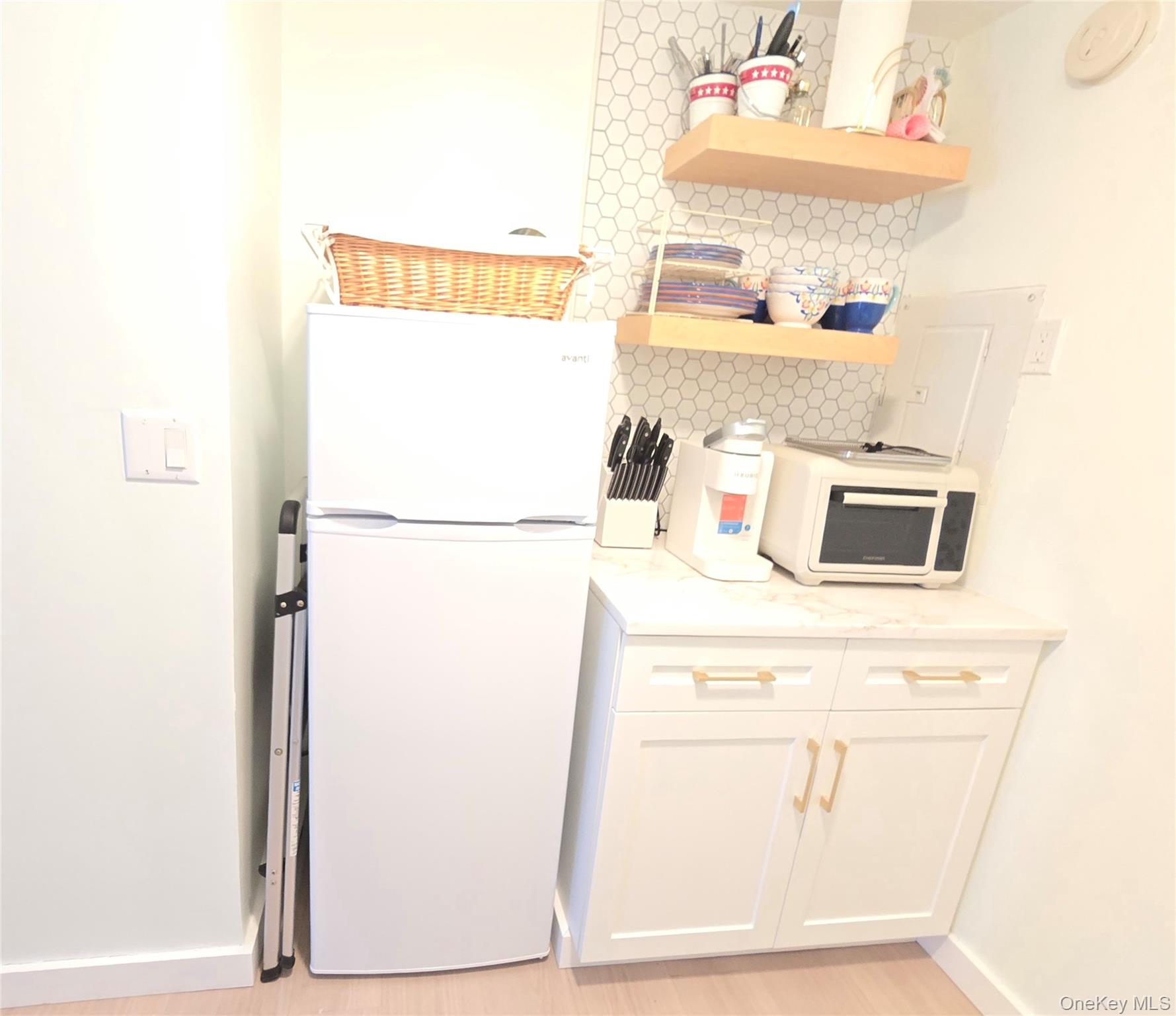 585 Dune Road, Unit L10 Westhampton, NY 11978 - Photo 14 of 25 Compact kitchen area featuring a white refrigerator, white shaker-style cabinetry with gold-tone hardware, and a light-colored countertop