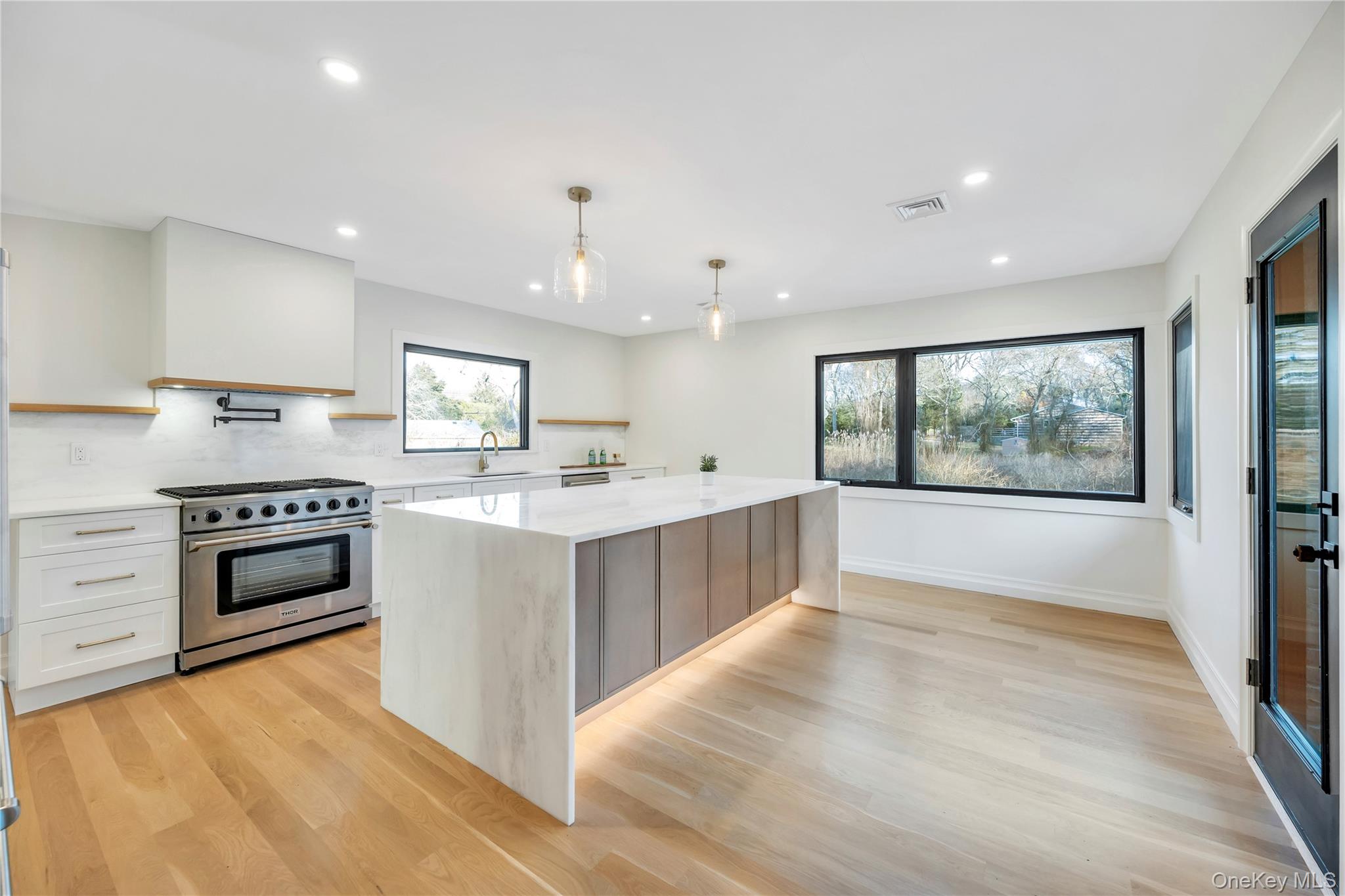 10 Lenape Road Southampton, NY 11968 - Photo 6 of 16 Kitchen featuring high end stainless steel range oven, hanging light fixtures, light stone counters, white cabinetry, and light wood finished floors