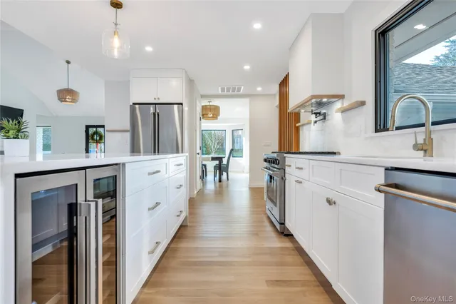 a large white kitchen with stainless steel appliances granite countertop a stove a sink dishwasher and white cabinets with wooden floor