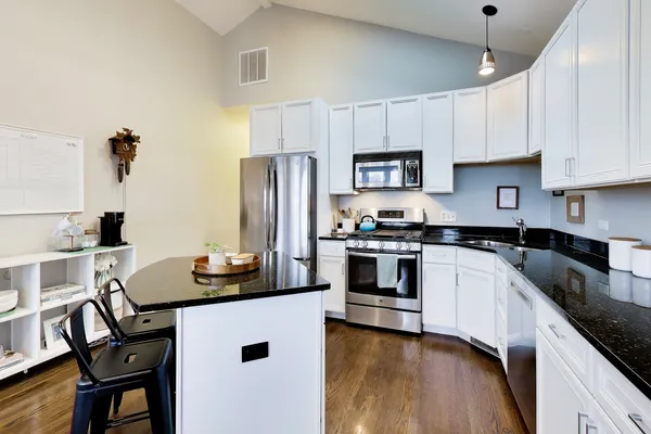 a kitchen with stainless steel appliances kitchen island granite countertop a table chairs stove and white cabinets