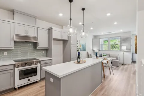 a kitchen with stainless steel appliances kitchen island granite countertop a refrigerator a sink dishwasher a stove a dining table and chairs with wooden floor