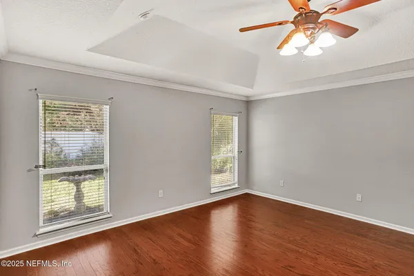 an empty room with wooden floor fan and windows
