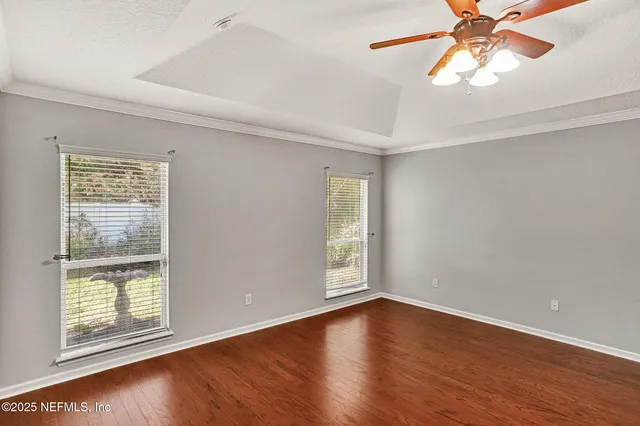 an empty room with wooden floor fan and windows