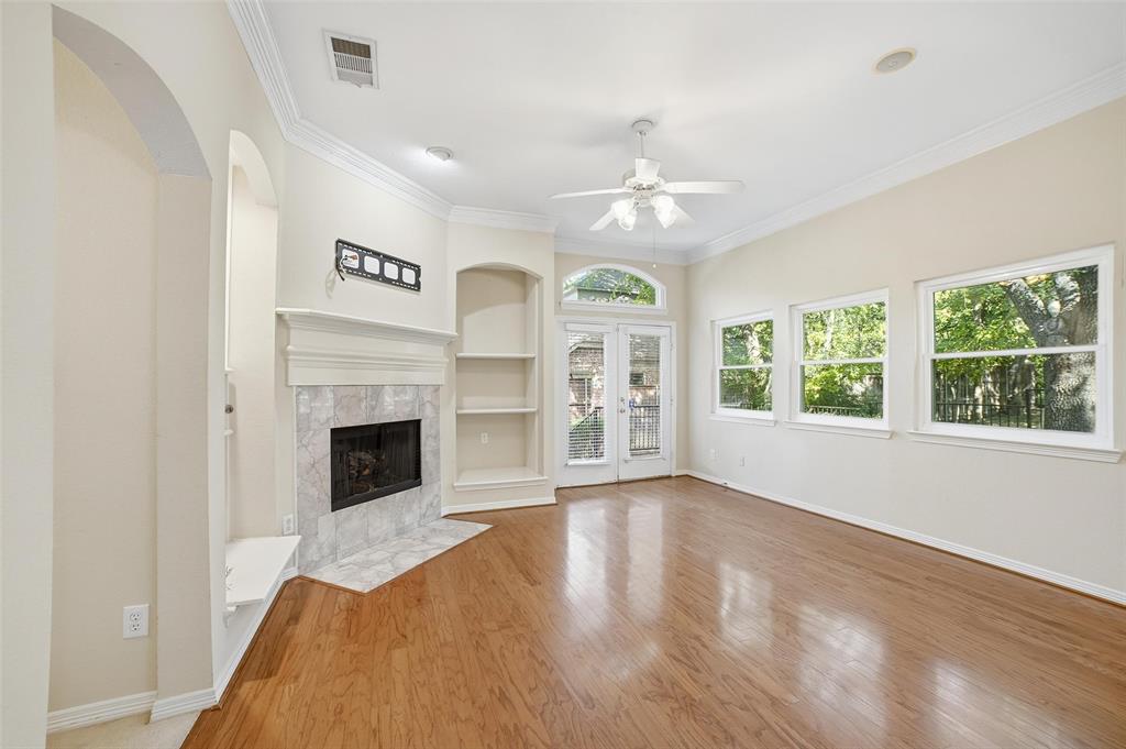 7909 Enclave Way Dallas, TX 75218 - Photo 10 of 21 Unfurnished living room with built in shelves, crown molding, wood finished floors, a premium fireplace, and ceiling fan