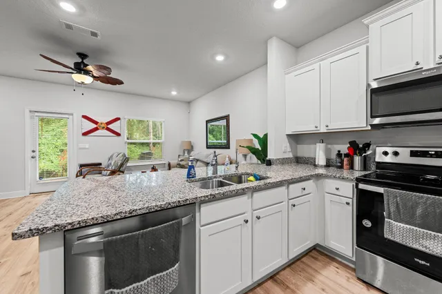 a kitchen with stainless steel appliances granite countertop a sink dishwasher a stove and a refrigerator with wooden floor