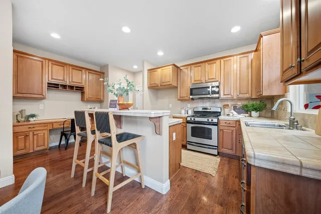 a kitchen with stainless steel appliances granite countertop a stove top oven a sink dishwasher a dining table and chairs with wooden floor