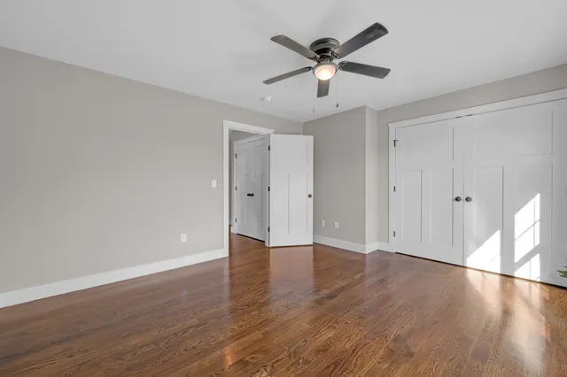an empty room with wooden floor fan and windows