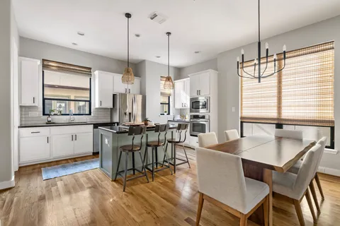 a kitchen with stainless steel appliances granite countertop a stove a sink a refrigerator a dining table and chairs with wooden floor