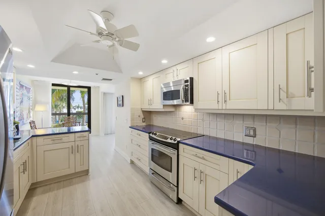 a kitchen with stainless steel appliances granite countertop white cabinets a sink a stove a dining table and chairs