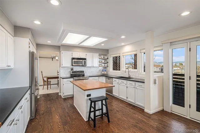 a kitchen with stainless steel appliances granite countertop a refrigerator a sink dishwasher a stove and white countertops with wooden floor