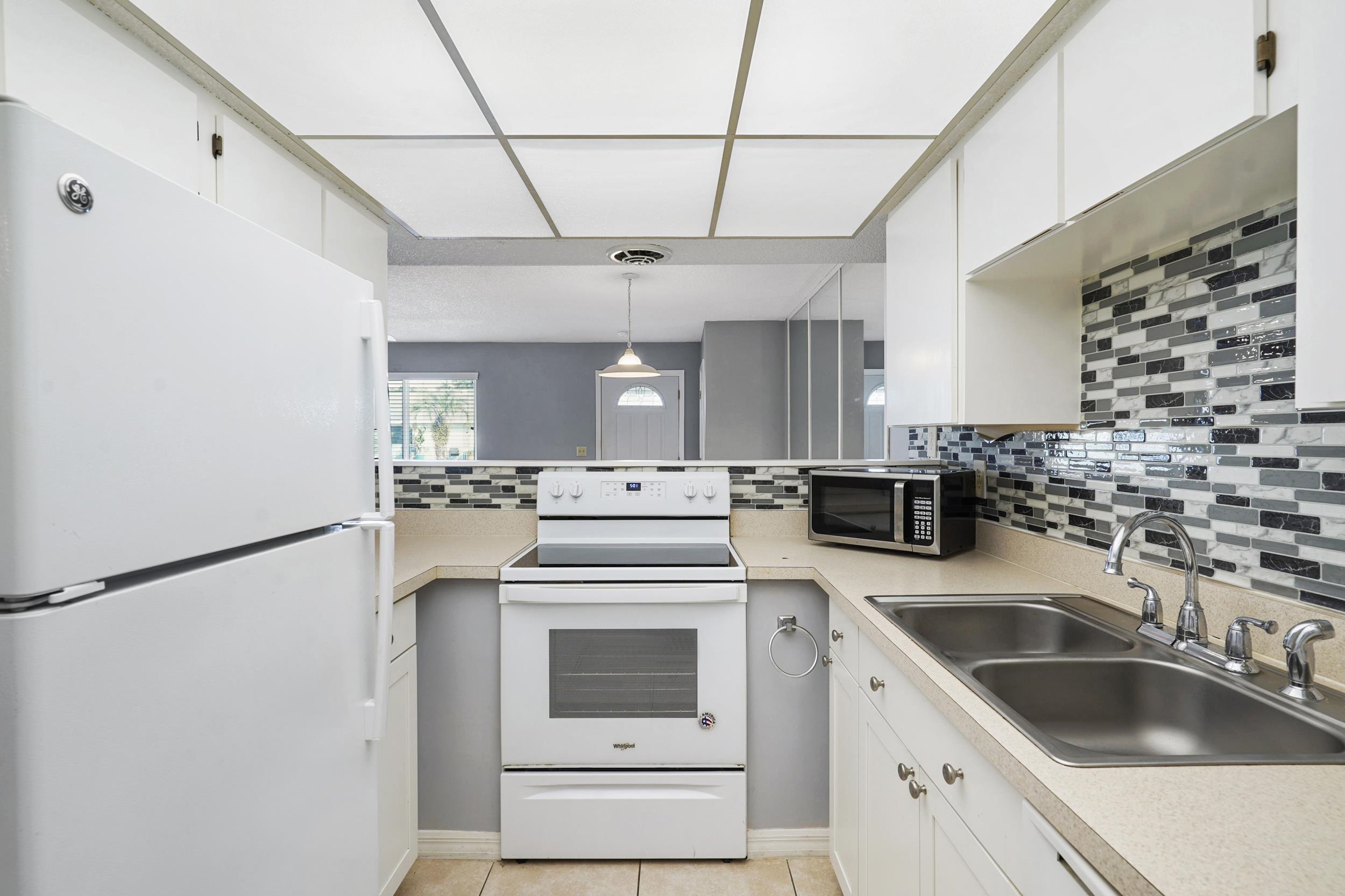 127 Rio Del Mar Street, Unit C St. Augustine, FL 32080 - Photo 7 of 29 Kitchen featuring white appliances, light countertops, decorative backsplash, and white cabinetry