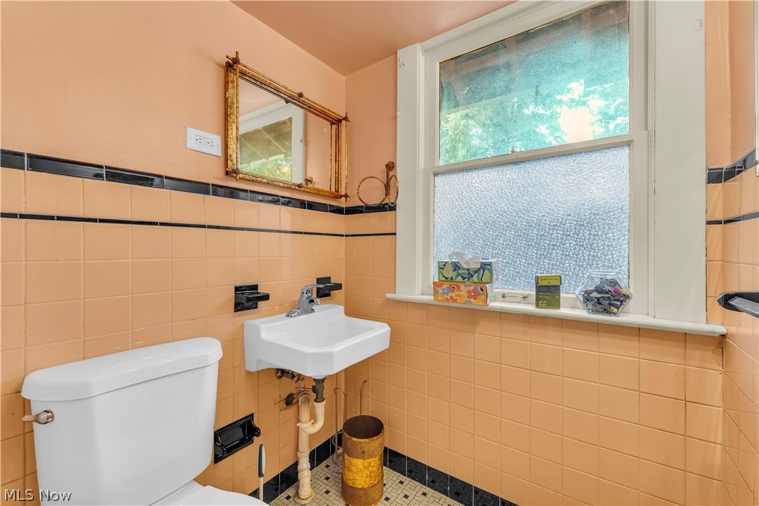 17406 Nottingham Road Cleveland, OH 44119 - Photo 17 of 45 Pedestal sink with chrome faucet, ceramic wall tiles with black accent bands, and a window featuring frosted glass