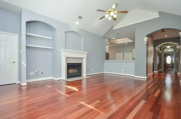 an empty room with wooden floor a ceiling fan a fireplace and windows