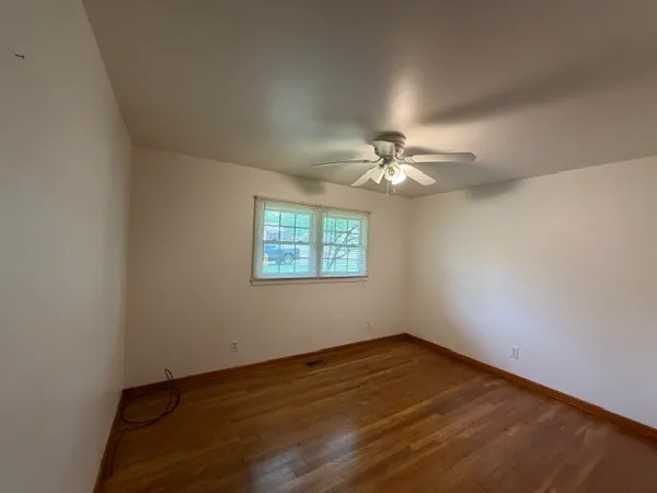 an empty room with wooden floor chandelier fan and windows