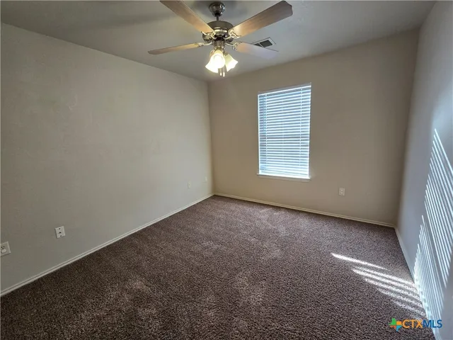 an empty room with a chandelier fan and windows