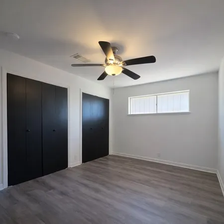 a view of an empty room with wooden floor and a ceiling fan
