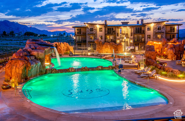 Pool at dusk featuring a patio, a mountain view, a pool with connected hot tub, and a balcony