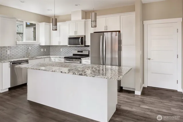 a kitchen with stainless steel appliances granite countertop a refrigerator a stove a sink and white cabinets with wooden floor