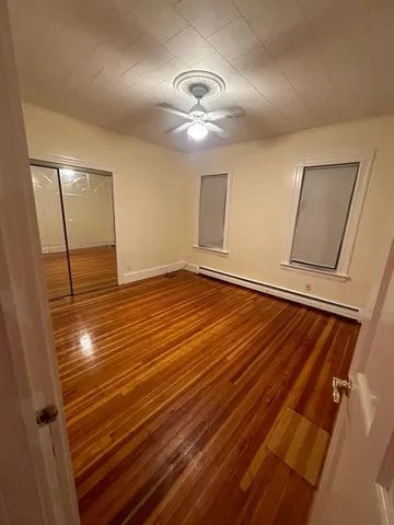 a view of an empty room with wooden floor and a ceiling fan