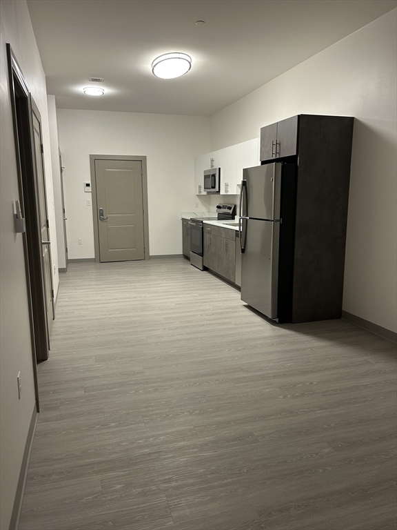 626 Main Street, Unit 201 Dennis, MA 02639 - Photo 4 of 18 a view of a refrigerator in kitchen and an empty room with wooden floor