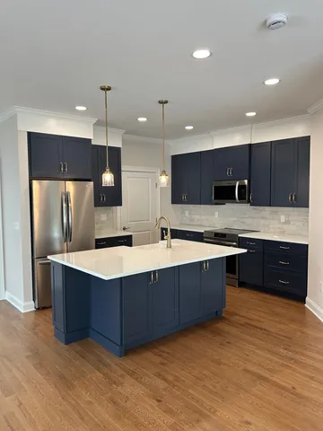 a large kitchen with stainless steel appliances kitchen island granite countertop a large counter top a sink dishwasher a refrigerator and a oven with wooden floor