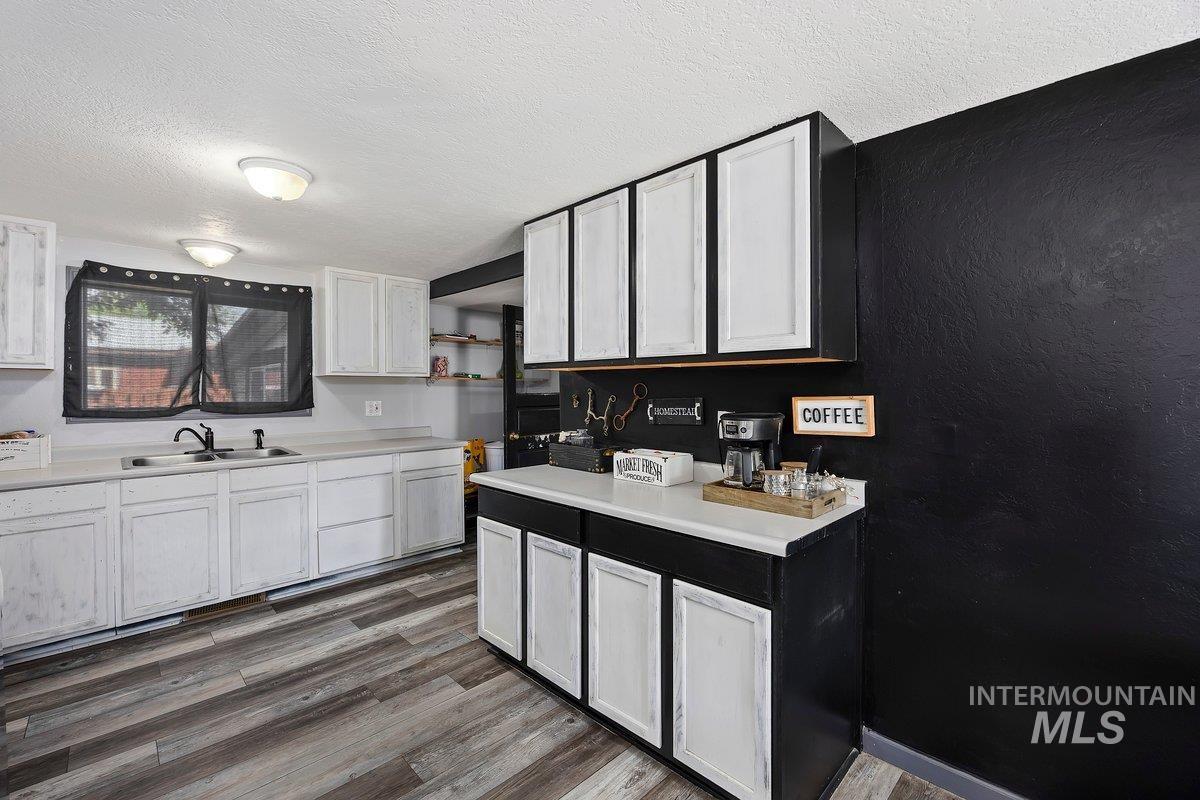 418 South Date Street Shoshone, ID 83352 - Photo 13 of 36 Kitchen featuring white upper and lower cabinetry, a dual-basin sink with a gooseneck faucet, light-toned countertops, and wood-finish flooring