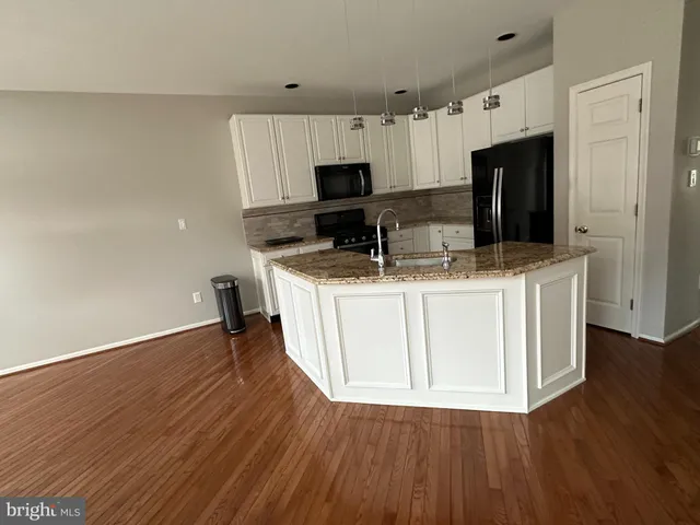 a kitchen with granite countertop a sink dishwasher stove and white cabinets with wooden floor