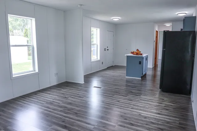 a view of a refrigerator in kitchen and an empty room with wooden floor