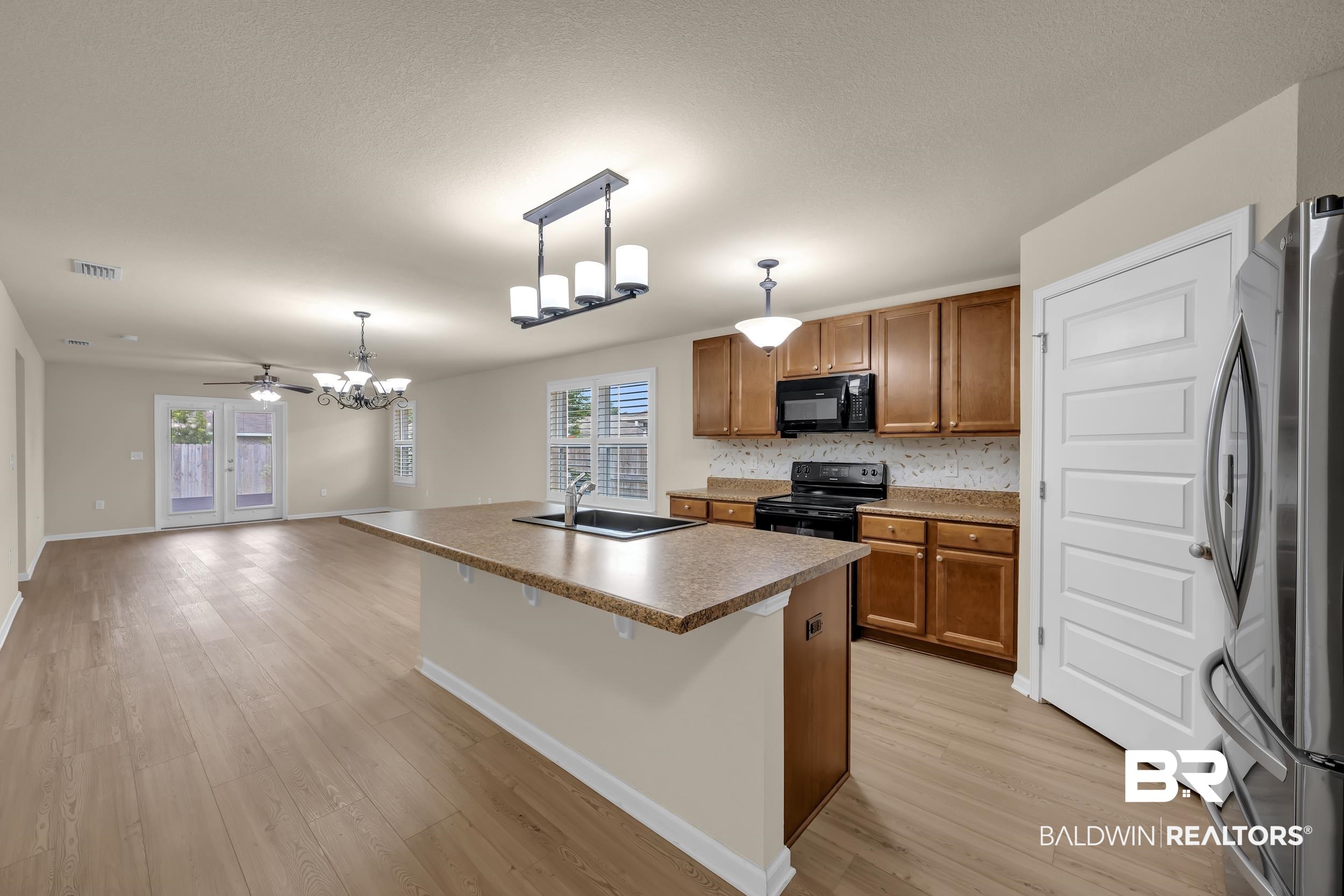 1704 Abbey Loop Foley, AL 36535 - Photo 9 of 38 Open-concept living area featuring wood-finish flooring, a kitchen island with integrated sink, wood cabinetry, stainless steel refrigerator, and glass patio doors