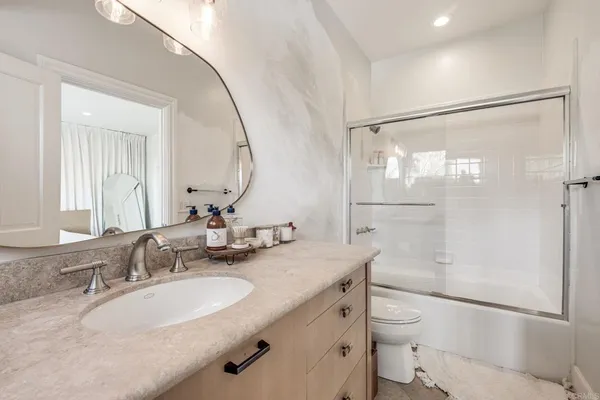 a bathroom with a granite countertop sink a toilet a mirror and shower