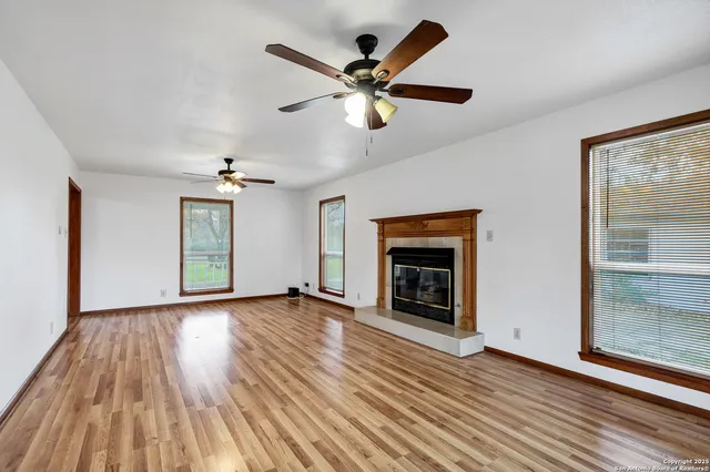an empty room with wooden floor chandelier fan and windows
