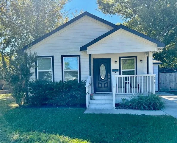 a view of a house with brick walls and a yard with plants and large trees
