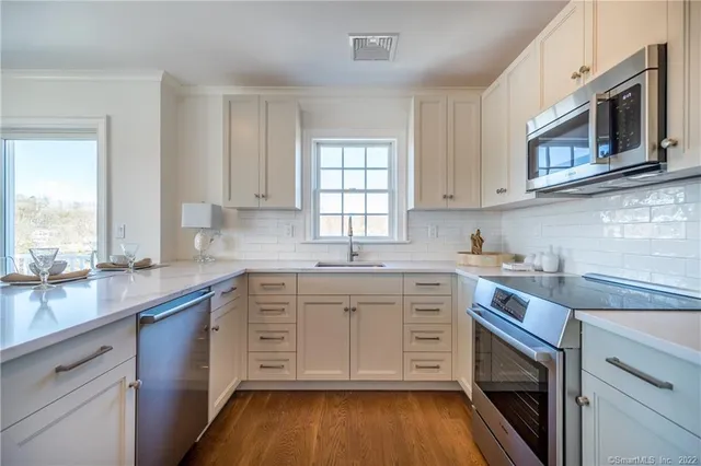 a kitchen with white cabinets appliances a sink and a window