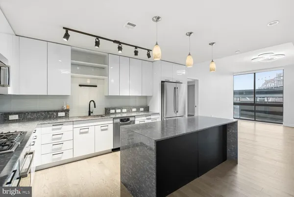 a kitchen with stainless steel appliances granite countertop a refrigerator a sink a stove and white cabinets with wooden floor