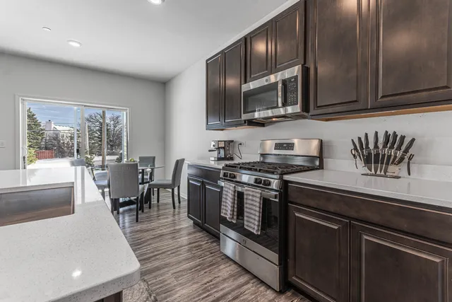 a kitchen with stainless steel appliances granite countertop a refrigerator a stove top oven a sink dishwasher a dining table and chairs with wooden floor