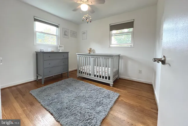 a view of a bedroom with wooden floor & a ceiling fan